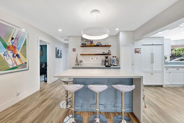 kitchen with paneled refrigerator, white cabinets, a breakfast bar area, and light wood-type flooring