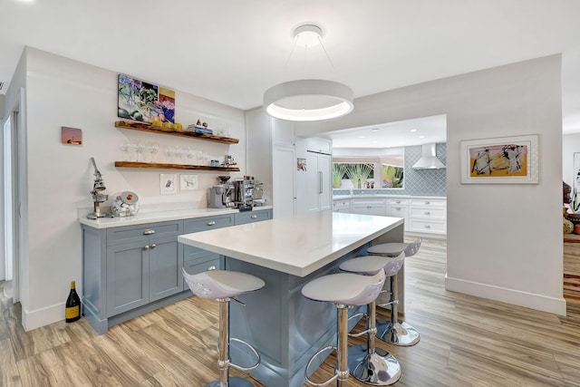 kitchen with a kitchen breakfast bar, decorative backsplash, light hardwood / wood-style floors, a kitchen island, and wall chimney range hood