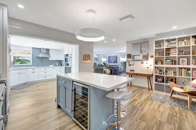 kitchen with beverage cooler, white cabinetry, wall chimney range hood, light hardwood / wood-style flooring, and double oven