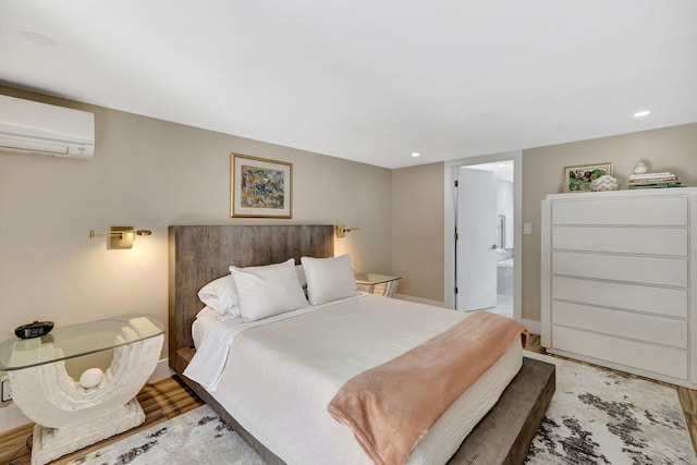 bedroom featuring light hardwood / wood-style flooring, connected bathroom, and a wall mounted air conditioner