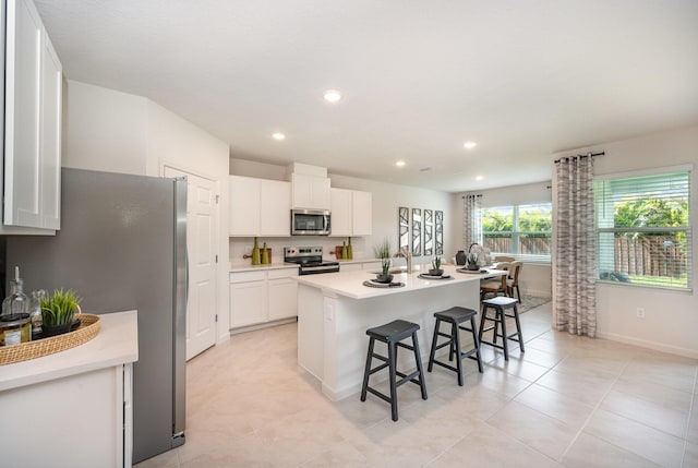 kitchen with a kitchen bar, a center island with sink, appliances with stainless steel finishes, white cabinets, and light countertops