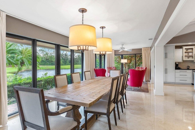 dining space with ceiling fan with notable chandelier and a water view