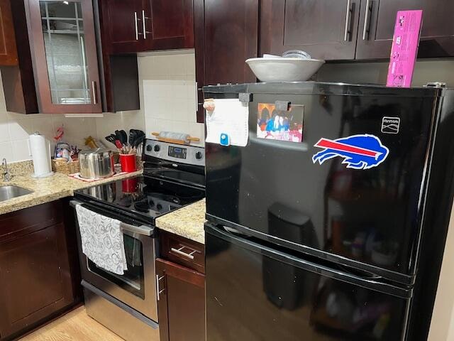 kitchen featuring light stone counters, sink, stainless steel electric range, backsplash, and black refrigerator