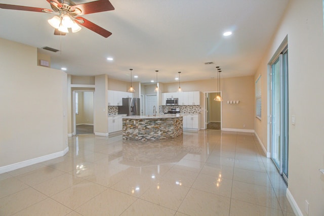 kitchen featuring a center island with sink, appliances with stainless steel finishes, white cabinets, pendant lighting, and decorative backsplash