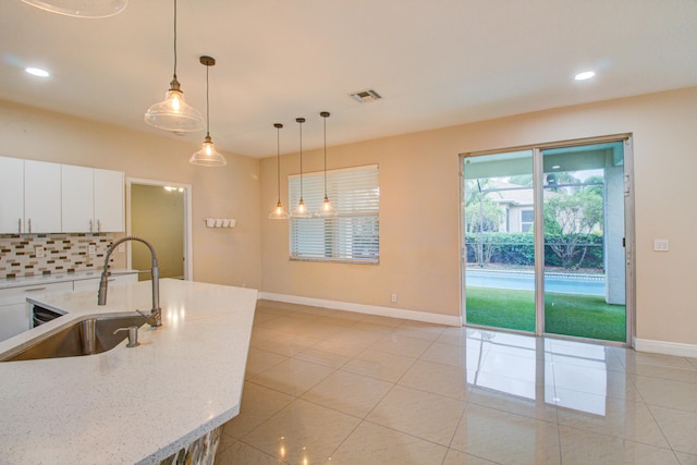 kitchen with sink, light stone counters, tasteful backsplash, white cabinets, and pendant lighting