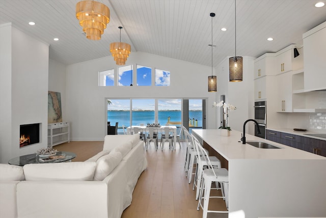 kitchen featuring a water view, an island with sink, wooden ceiling, decorative light fixtures, and sink