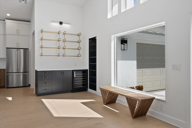 interior space with light hardwood / wood-style flooring, white cabinets, a towering ceiling, and stainless steel fridge