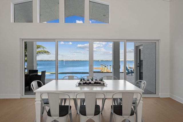 dining space with a towering ceiling, a water view, and light hardwood / wood-style floors