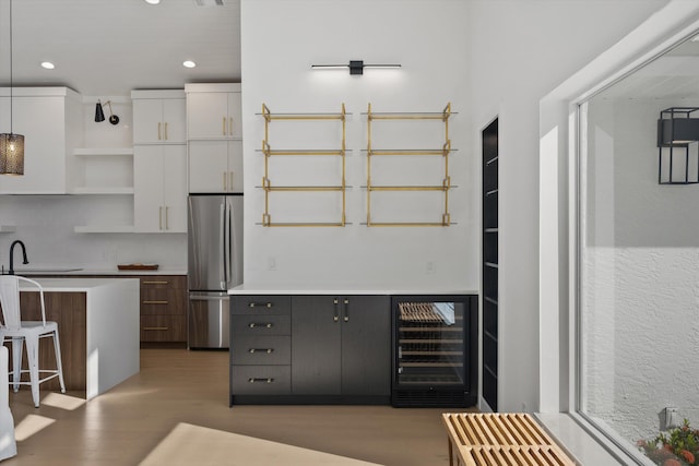 kitchen with hanging light fixtures, stainless steel fridge, white cabinetry, light wood-type flooring, and beverage cooler