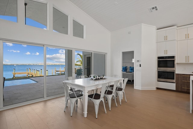 dining room with light hardwood / wood-style flooring, a water view, high vaulted ceiling, and crown molding