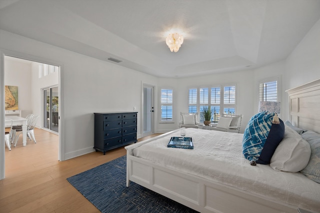 bedroom with a raised ceiling, light hardwood / wood-style floors, and multiple windows