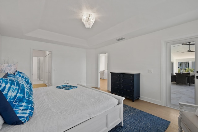 bedroom with a notable chandelier, a tray ceiling, ensuite bathroom, and hardwood / wood-style flooring