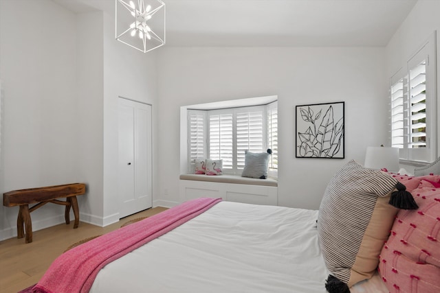 bedroom featuring light wood-type flooring, a chandelier, multiple windows, and lofted ceiling