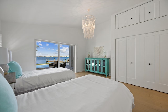 bedroom with light hardwood / wood-style floors, access to exterior, a notable chandelier, vaulted ceiling, and a water view