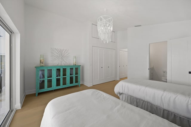 bedroom with ensuite bathroom, a closet, a chandelier, and hardwood / wood-style floors