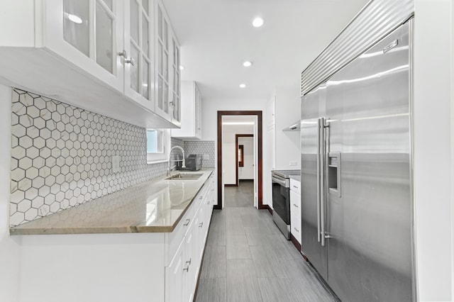 kitchen with light stone countertops, sink, stainless steel appliances, backsplash, and white cabinets