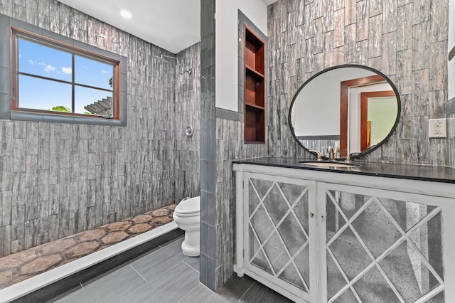 bathroom featuring a tile shower, tile patterned flooring, toilet, vanity, and tile walls