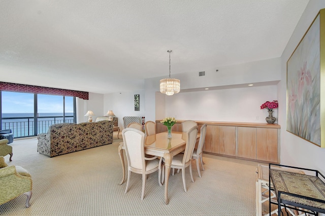 dining area featuring a water view, a textured ceiling, light colored carpet, and a chandelier