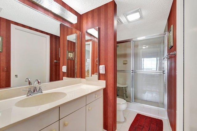 bathroom featuring a shower with shower door, vanity, a textured ceiling, tile patterned flooring, and toilet