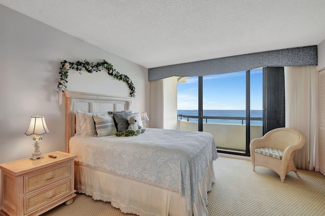 bedroom with a water view, a textured ceiling, light colored carpet, and access to outside