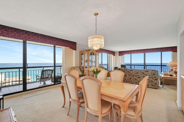 dining space with light carpet, a water view, a textured ceiling, and a chandelier