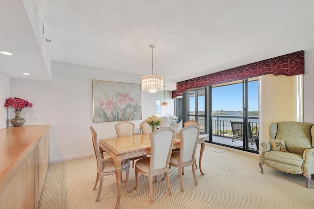 carpeted dining area featuring a water view, a textured ceiling, and a chandelier