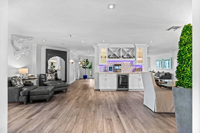 bar with ornamental molding, light wood-type flooring, beverage cooler, and white cabinetry