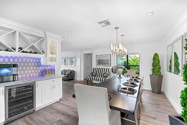 dining room featuring ornamental molding, light wood-type flooring, beverage cooler, and a chandelier