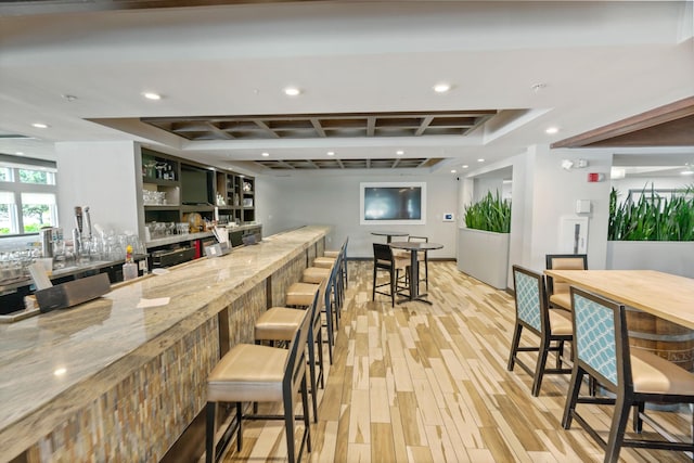 kitchen featuring a raised ceiling, light hardwood / wood-style floors, light stone counters, and a breakfast bar