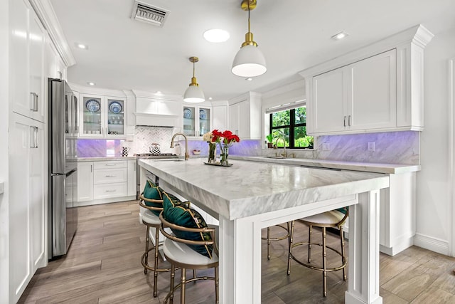 kitchen featuring hanging light fixtures, white cabinets, stainless steel fridge, and light wood-type flooring