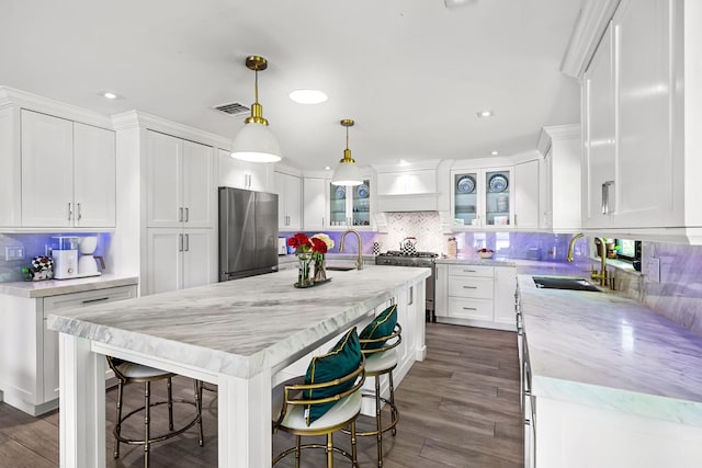 kitchen featuring sink, hanging light fixtures, appliances with stainless steel finishes, an island with sink, and white cabinetry