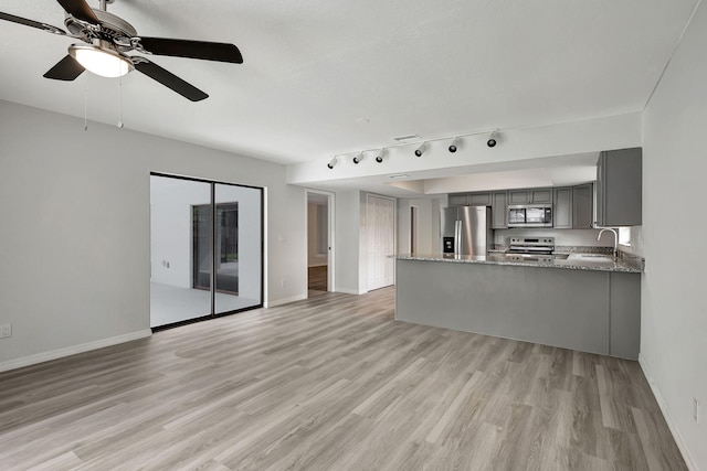 interior space featuring gray cabinets, light hardwood / wood-style floors, kitchen peninsula, stainless steel appliances, and stone countertops