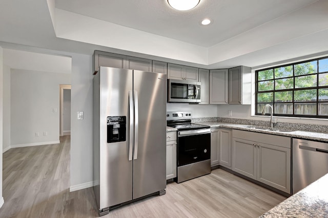 kitchen featuring sink, gray cabinetry, light hardwood / wood-style flooring, stainless steel appliances, and light stone countertops