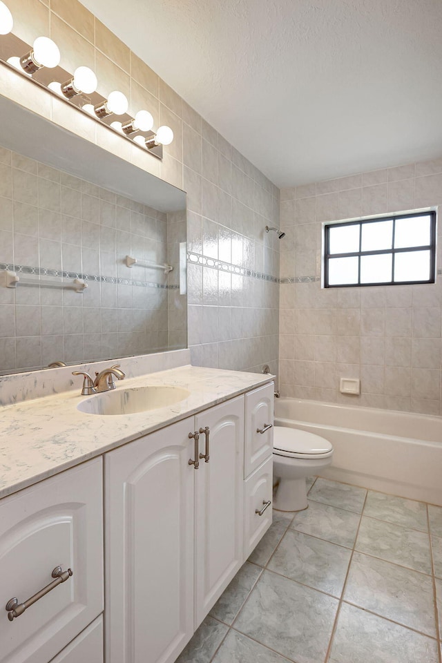 full bathroom with tile walls, tiled shower / bath combo, vanity, and toilet