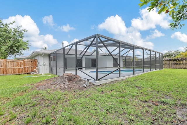 rear view of house with glass enclosure, a yard, and a fenced in pool