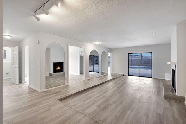 unfurnished living room with a textured ceiling, light hardwood / wood-style floors, and rail lighting