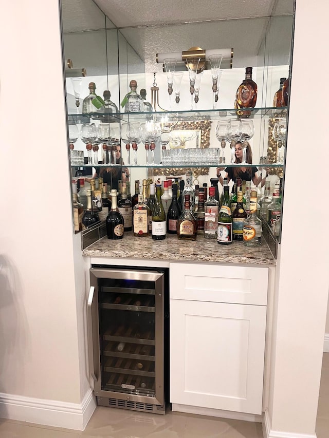 bar with wine cooler, white cabinetry, and stone counters