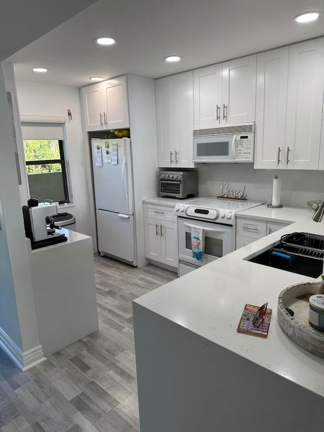 kitchen with light hardwood / wood-style floors, white appliances, and white cabinets