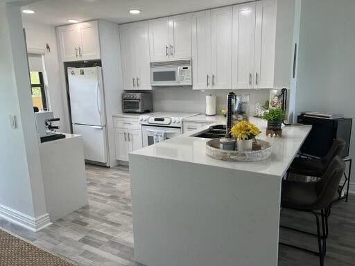 kitchen with a kitchen breakfast bar, white cabinets, white appliances, kitchen peninsula, and light hardwood / wood-style flooring