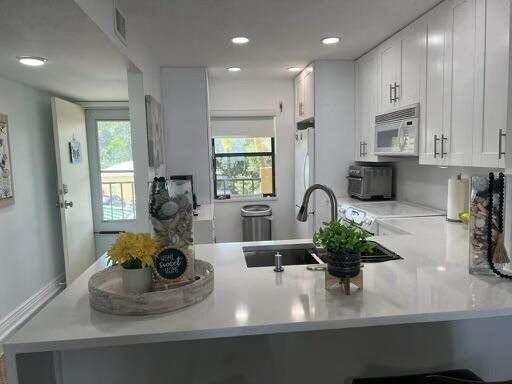 kitchen with sink, kitchen peninsula, white appliances, and white cabinetry