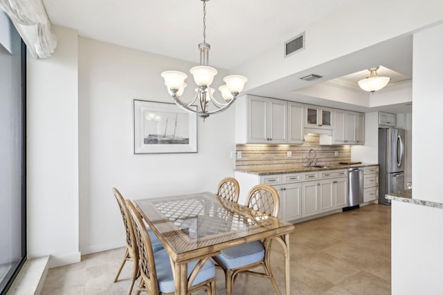 dining space with a notable chandelier, ornamental molding, sink, and a raised ceiling