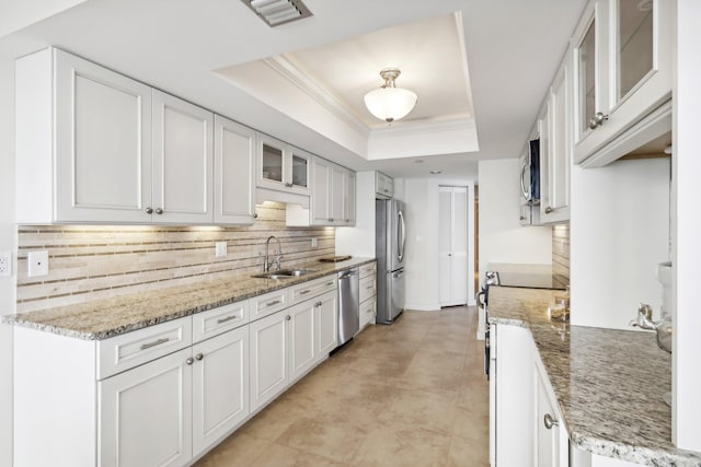 kitchen featuring light stone counters, a raised ceiling, appliances with stainless steel finishes, white cabinetry, and sink