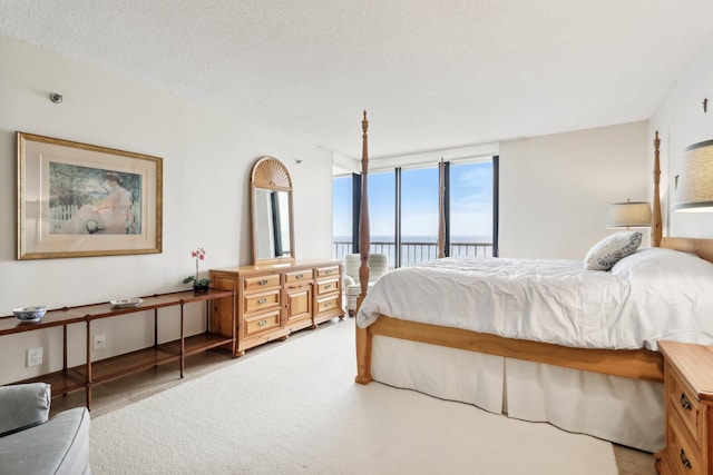 bedroom with access to exterior, a water view, a textured ceiling, and floor to ceiling windows