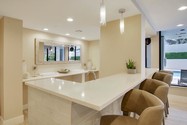 kitchen with light hardwood / wood-style floors, light stone counters, hanging light fixtures, and plenty of natural light