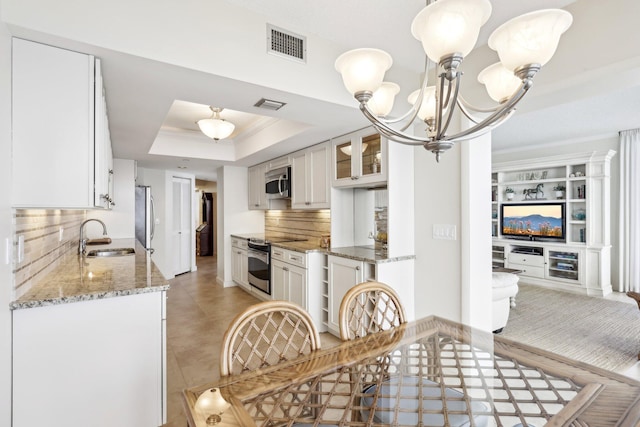 kitchen with white cabinets, tasteful backsplash, a raised ceiling, appliances with stainless steel finishes, and sink