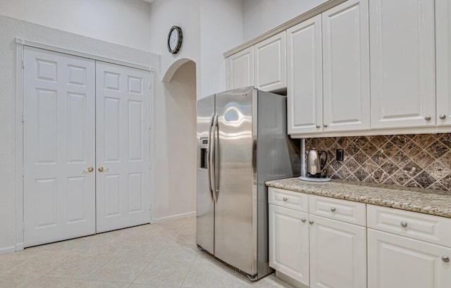 kitchen with light stone counters, stainless steel refrigerator with ice dispenser, light tile patterned floors, and decorative backsplash