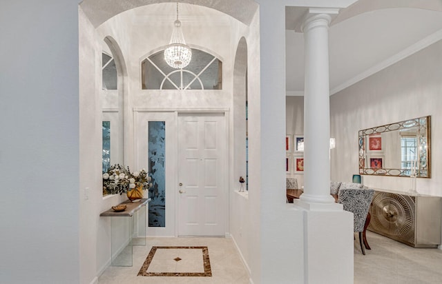 tiled foyer featuring ornate columns, ornamental molding, and a chandelier