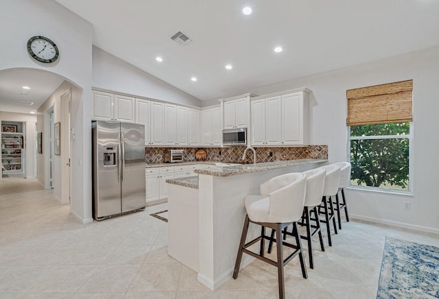 kitchen with appliances with stainless steel finishes, vaulted ceiling, a kitchen breakfast bar, and white cabinets