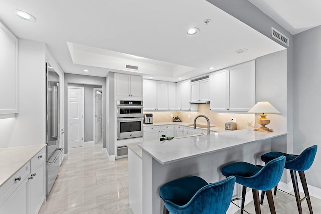 kitchen featuring kitchen peninsula, appliances with stainless steel finishes, decorative backsplash, white cabinets, and a breakfast bar area