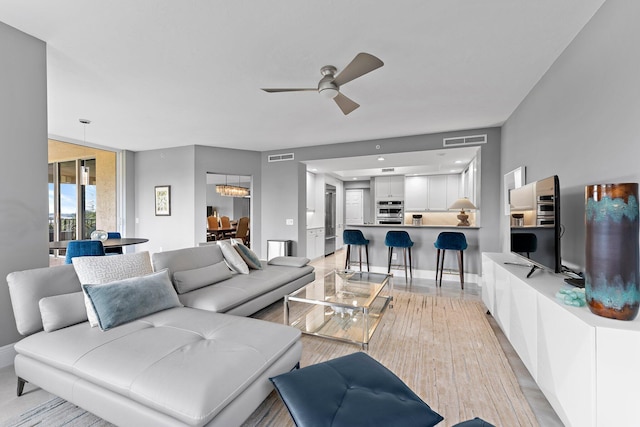 living room featuring ceiling fan with notable chandelier and light wood-type flooring